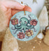 a hand holding a christmas ornament with an octopus holding presents