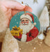 a hand holding a christmas ornament with a santa clause on it