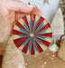a hand holding a red, yellow and blue ornament