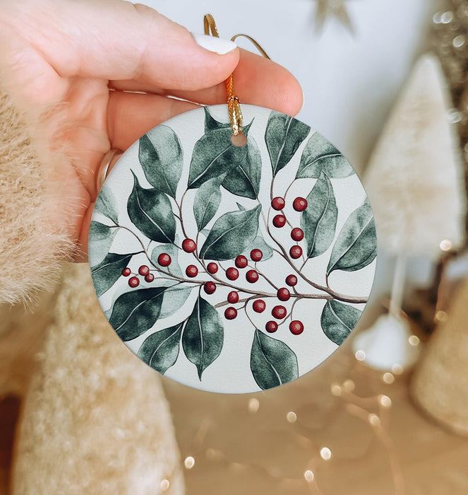 a hand holding a ceramic ornament with holly and berries