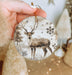 a hand holding a christmas ornament with a deer on it