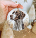a hand holding a christmas ornament with a dog on it