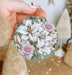 a person holding a christmas ornament with flowers on it