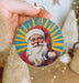 a hand holding a christmas ornament with a santa clause on it