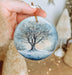 a hand holding a glass ornament with a tree on it