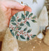 a hand holding a christmas ornament with berries on it