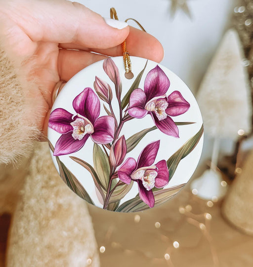 a hand holding a white ornament with pink flowers