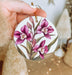 a hand holding a white ornament with pink flowers