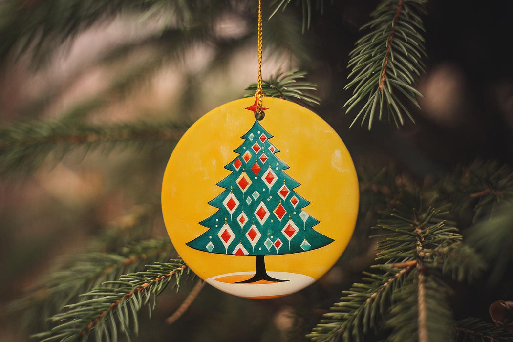 a ceramic christmas tree ornament hanging from a pine tree