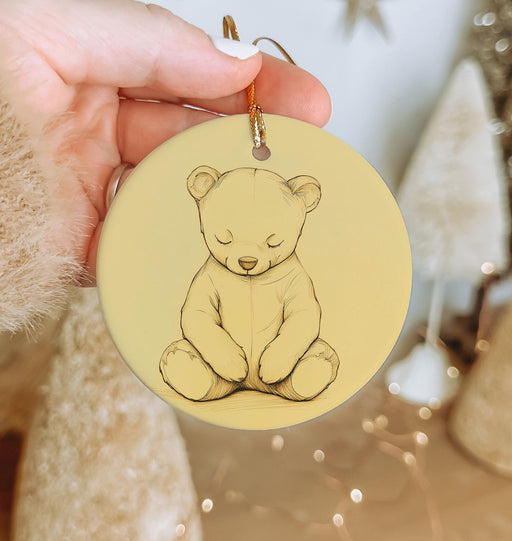 a hand holding a yellow ornament with a drawing of a teddy bear