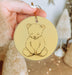a hand holding a yellow ornament with a drawing of a teddy bear