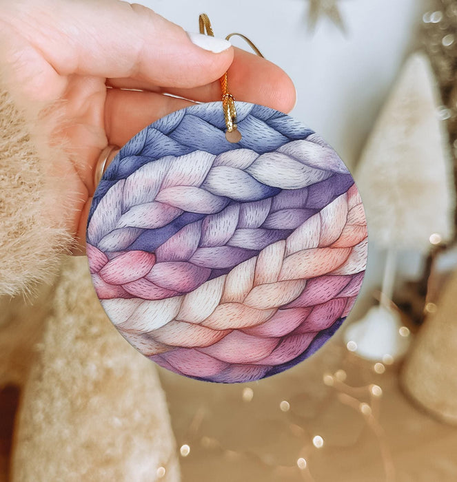 a hand holding a round ornament decorated with yarn