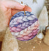 a hand holding a round ornament decorated with yarn