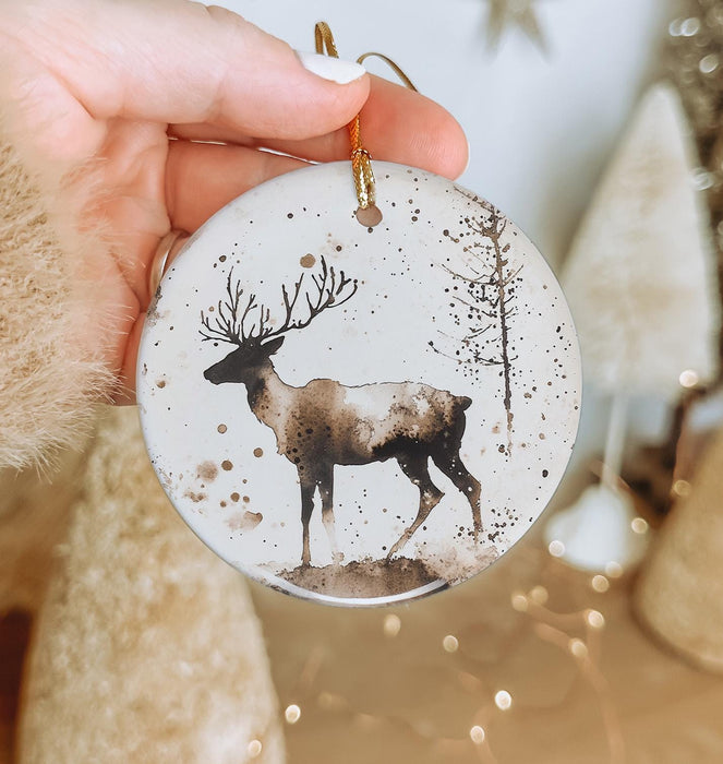 a hand holding a christmas ornament with a deer on it