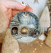 a hand holding a christmas ornament with a fireplace