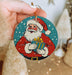 a hand holding a christmas ornament with a santa clause on it