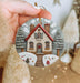 a hand holding a christmas ornament with a house on it