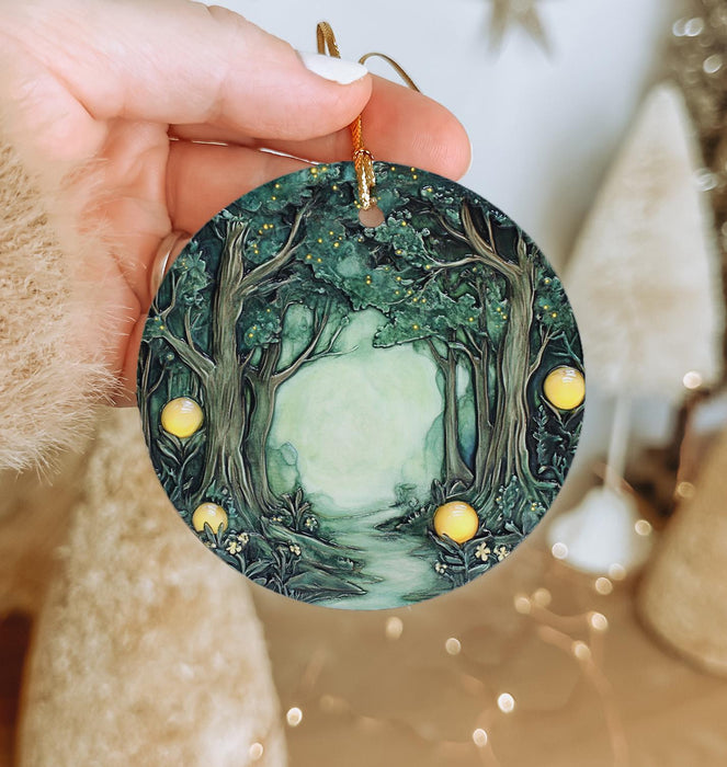 a hand holding a christmas ornament with a forest scene on it