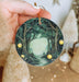 a hand holding a christmas ornament with a forest scene on it