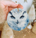 a hand holding an ornament with a picture of an owl on it