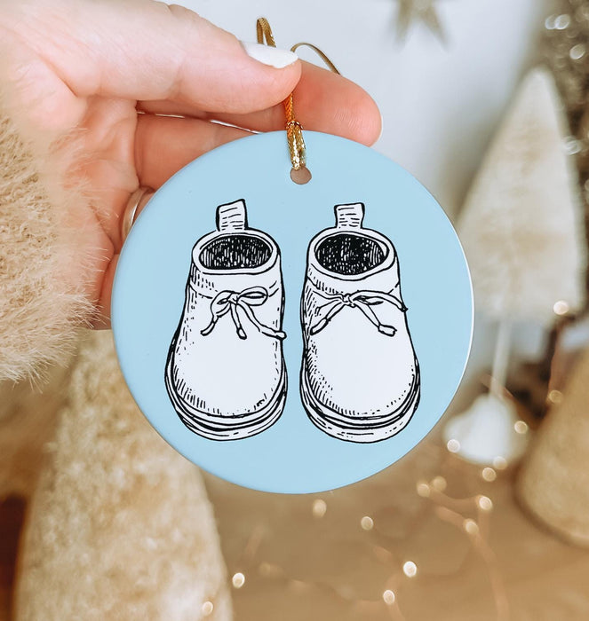 a hand holding a blue ornament with a pair of shoes on it