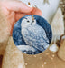a person holding a blue ornament with a white owl on it