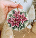a hand holding a christmas ornament with flowers on it