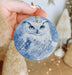 a hand holding an ornament with a picture of an owl on it