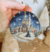 a hand holding a christmas ornament with a castle on it