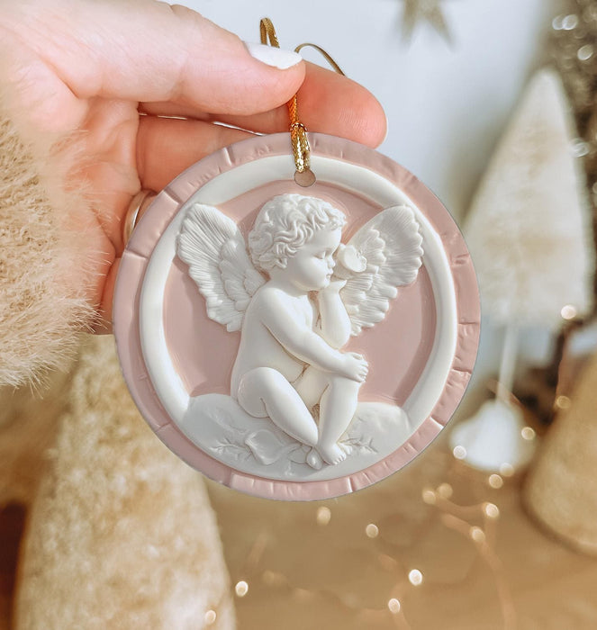 a hand holding a christmas ornament with an angel on it
