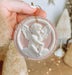 a hand holding a christmas ornament with an angel on it