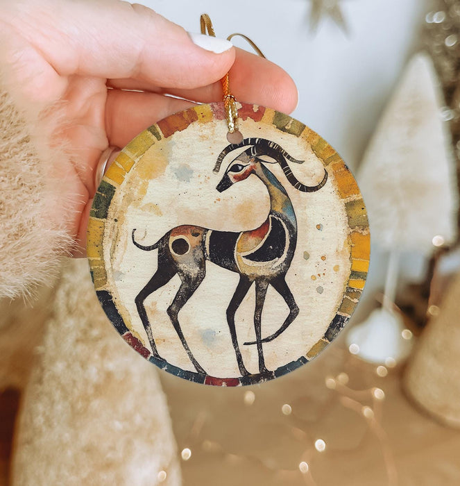 a hand holding a ceramic ornament with a picture of a deer