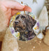 a hand holding a christmas ornament with a picture of a dog