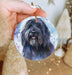 a hand holding a round ornament with a black dog on it