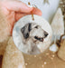 a hand holding a round ornament with a picture of a dog