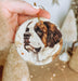 a hand holding a christmas ornament with a dog on it