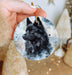 a hand holding a round ornament with a black dog on it