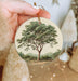 a hand holding a christmas ornament with a tree on it