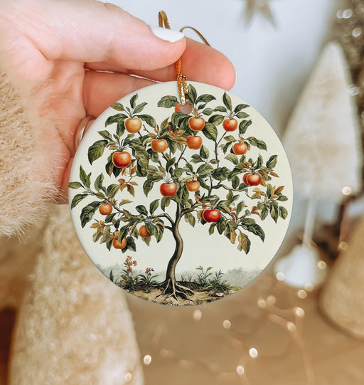 a hand holding a christmas ornament with an apple tree on it