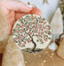 a hand holding a ceramic ornament with a tree on it