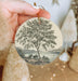 a person holding a christmas ornament with a tree on it