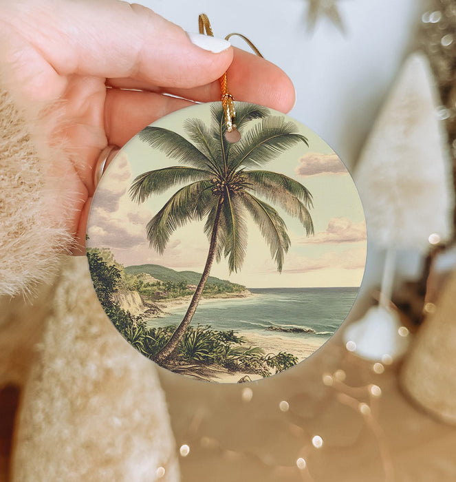 a person holding a christmas ornament with a painting of a palm tree
