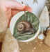 a hand holding a ceramic ornament with a snail on it