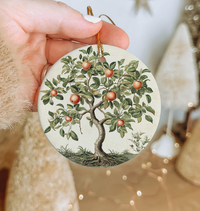 a hand holding a christmas ornament with an apple tree on it