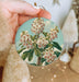 a person holding a round ornament with flowers on it