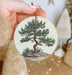 a person holding a christmas ornament with a tree on it