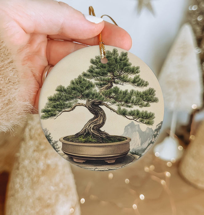 a person holding a christmas ornament with a bonsai tree on it