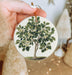 a person holding a christmas ornament with a tree on it