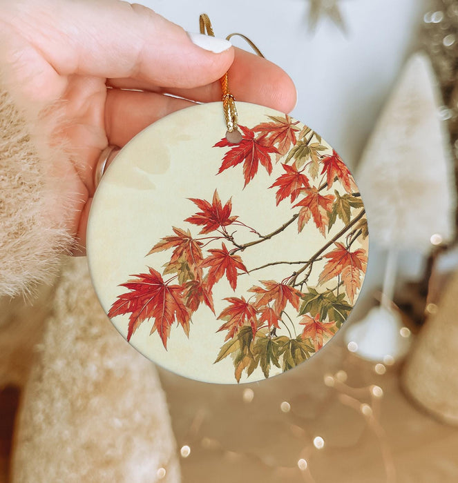 a hand holding a ceramic ornament with red leaves