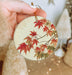 a hand holding a ceramic ornament with red leaves